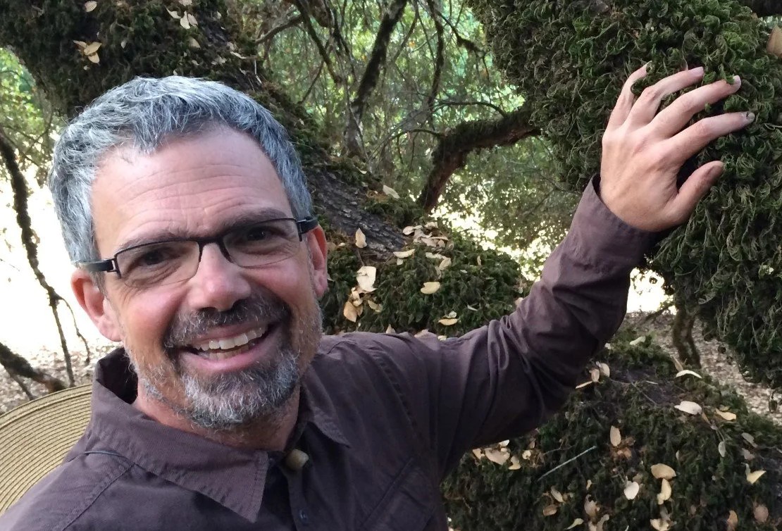 Dave with hand on large oak tree branch covered in moss.